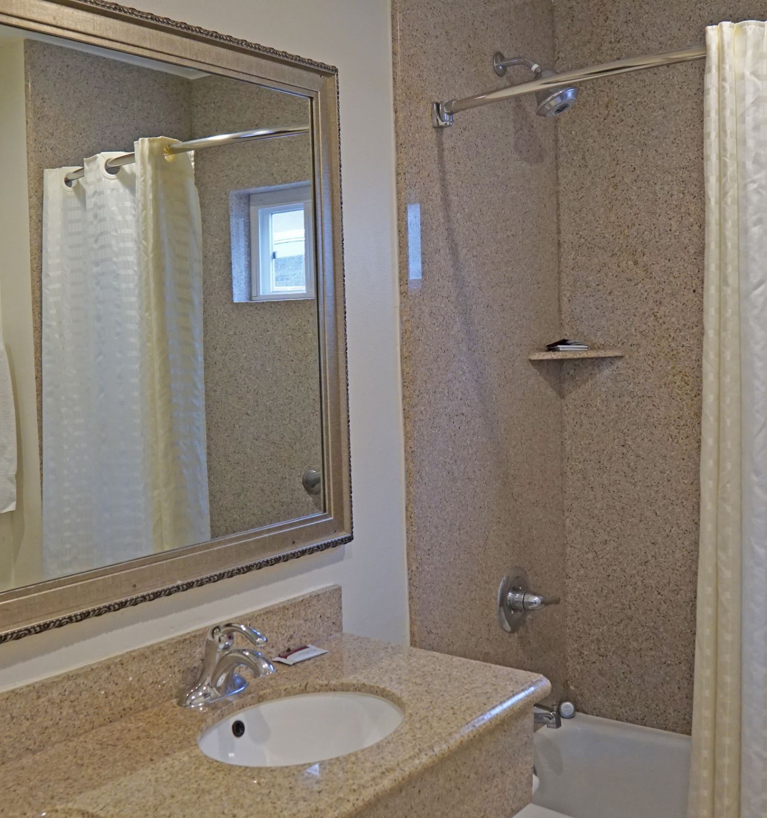 A bathroom with a sink, large mirror, hairdryer, towel, and a bathtub with a shower curtain. The walls are light-colored, and the countertop is beige.