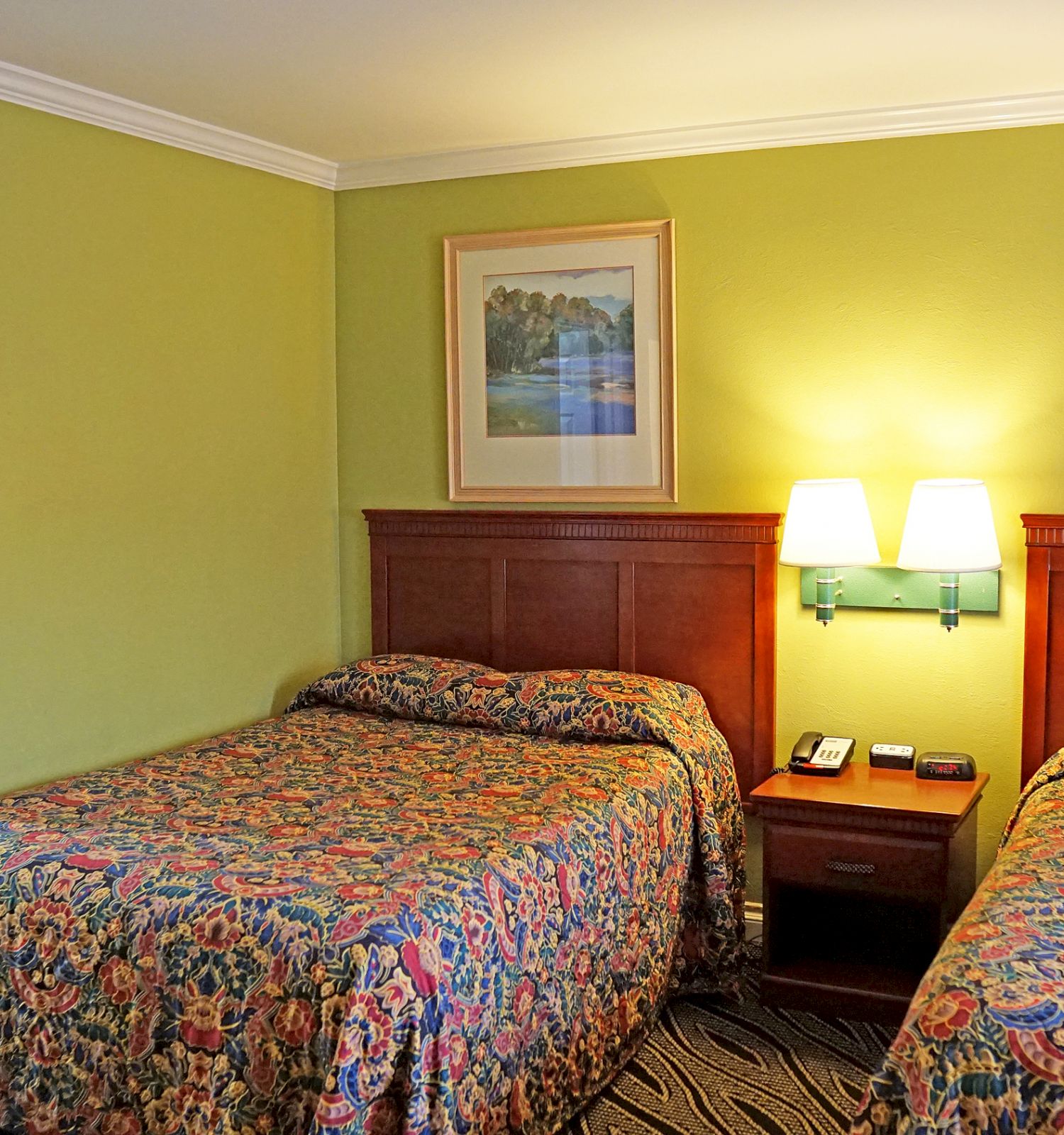 A hotel room with two beds, a nightstand, two wall paintings, and a connecting room.