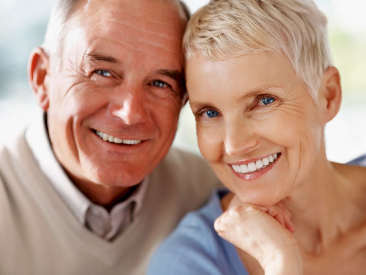 The image contains a smiling elderly couple with short hair, closely embracing each other while posing for the camera.