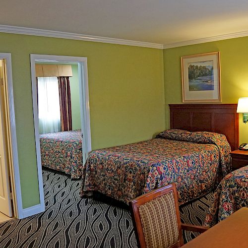 A hotel room with two double beds, a bathroom, a desk, and a lamp. The walls are green, and there are framed pictures above the beds.