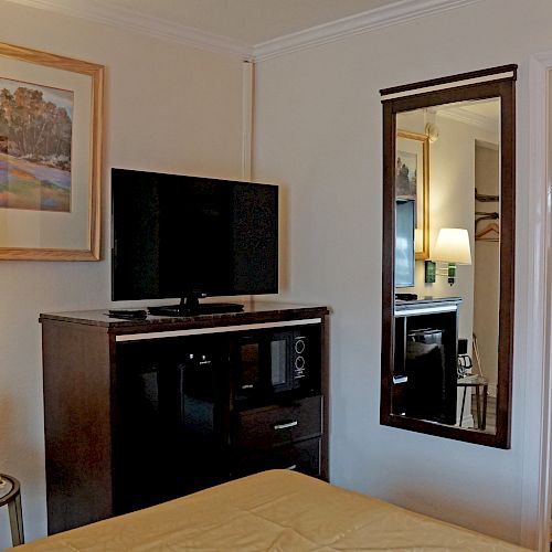 The image shows a hotel room with a bed, a TV on a dresser, a mirror, a nightstand with a lamp, and an open door to a bathroom.