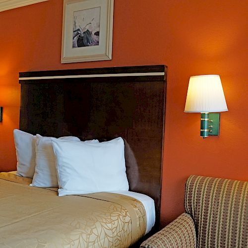 A cozy hotel room with a double bed, two bedside lamps, an armchair, and wall art above the headboard.