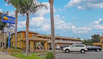 Image of a two-story motel with a parking lot, palm trees, and a sign reading 