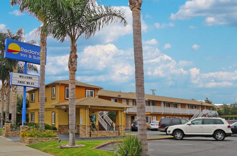 Image of a two-story motel with a parking lot, palm trees, and a sign reading 