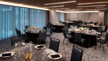 A banquet hall with round tables set for a formal event. Tables have black napkins, glassware, floral centerpieces, and candles, all ready for guests.