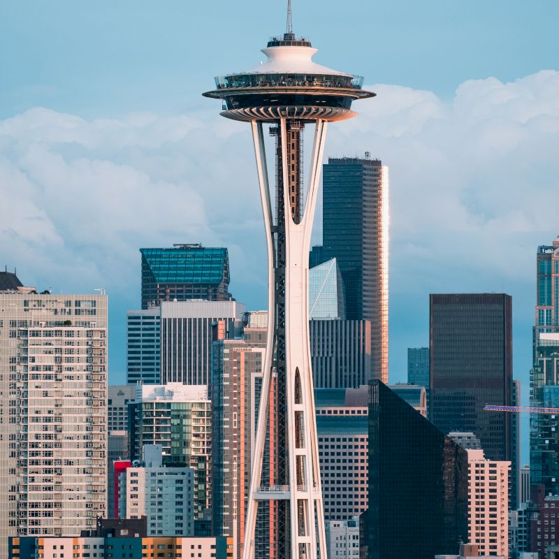 The image shows the Space Needle, an iconic observation tower, with the downtown Seattle skyline in the background, featuring various skyscrapers.