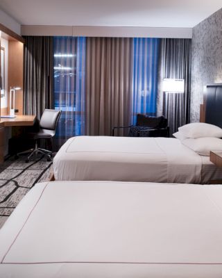 A modern hotel room with two double beds, a wall-mounted TV, a work desk, and a patterned wall and carpet.