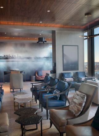 The image depicts a modern lounge area with comfortable seating, large windows offering a scenic view of the waterfront, and contemporary decor.