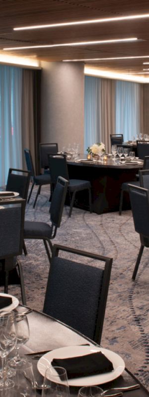 A banquet hall set up with round tables and chairs, adorned with elegant tableware and centerpieces, ready for a formal event or dinner.