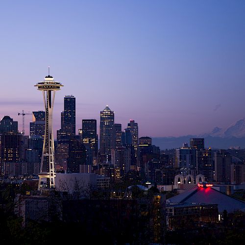 City skyline at dusk with a distinctive tower and a mountain in the background.