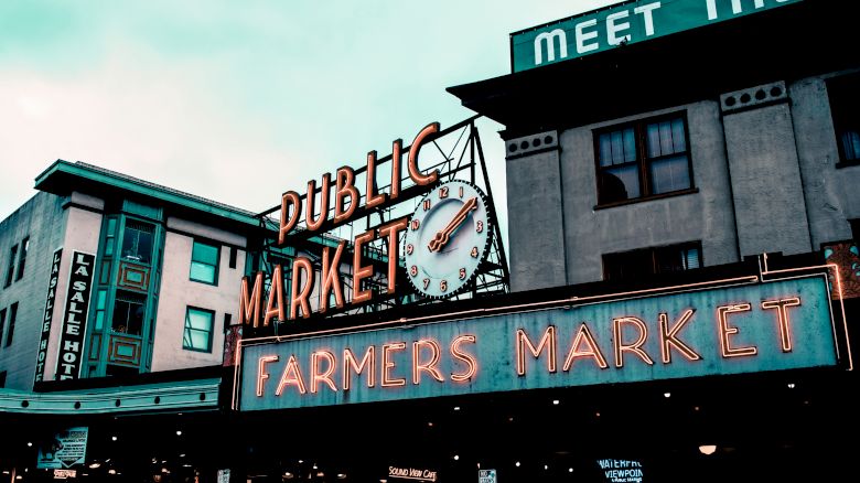 The image shows the exterior of a building with signs reading "Public Market" and "Farmers Market." There's a clock on the "Public Market" sign.