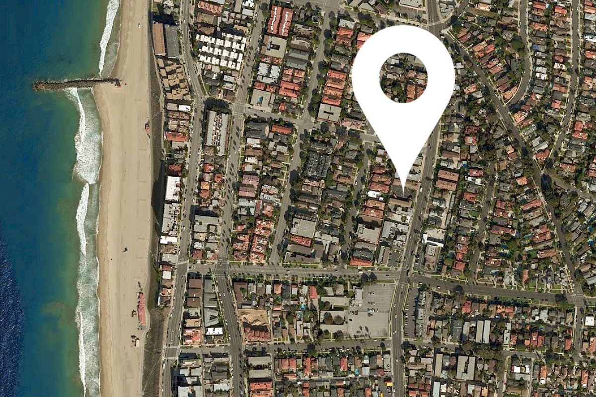 An aerial view of a coastal urban area highlighting a specific location with a map pin marker near the beach, with streets and buildings visible.